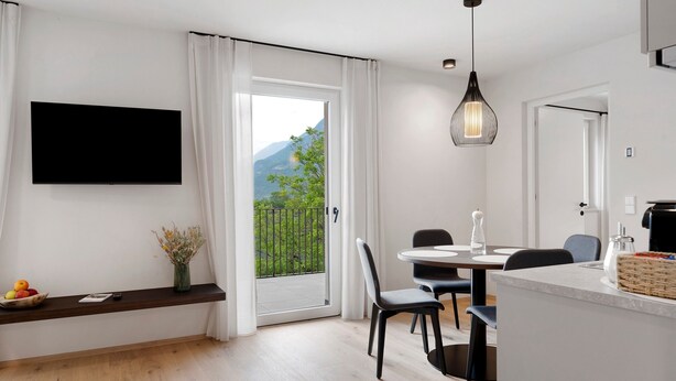 A modern kitchen with a dining area, a TV mounted on the wall, and a view of the outdoors. - Apartment 'Pink Lady' with Mountain View & Large Balcony (Lana)