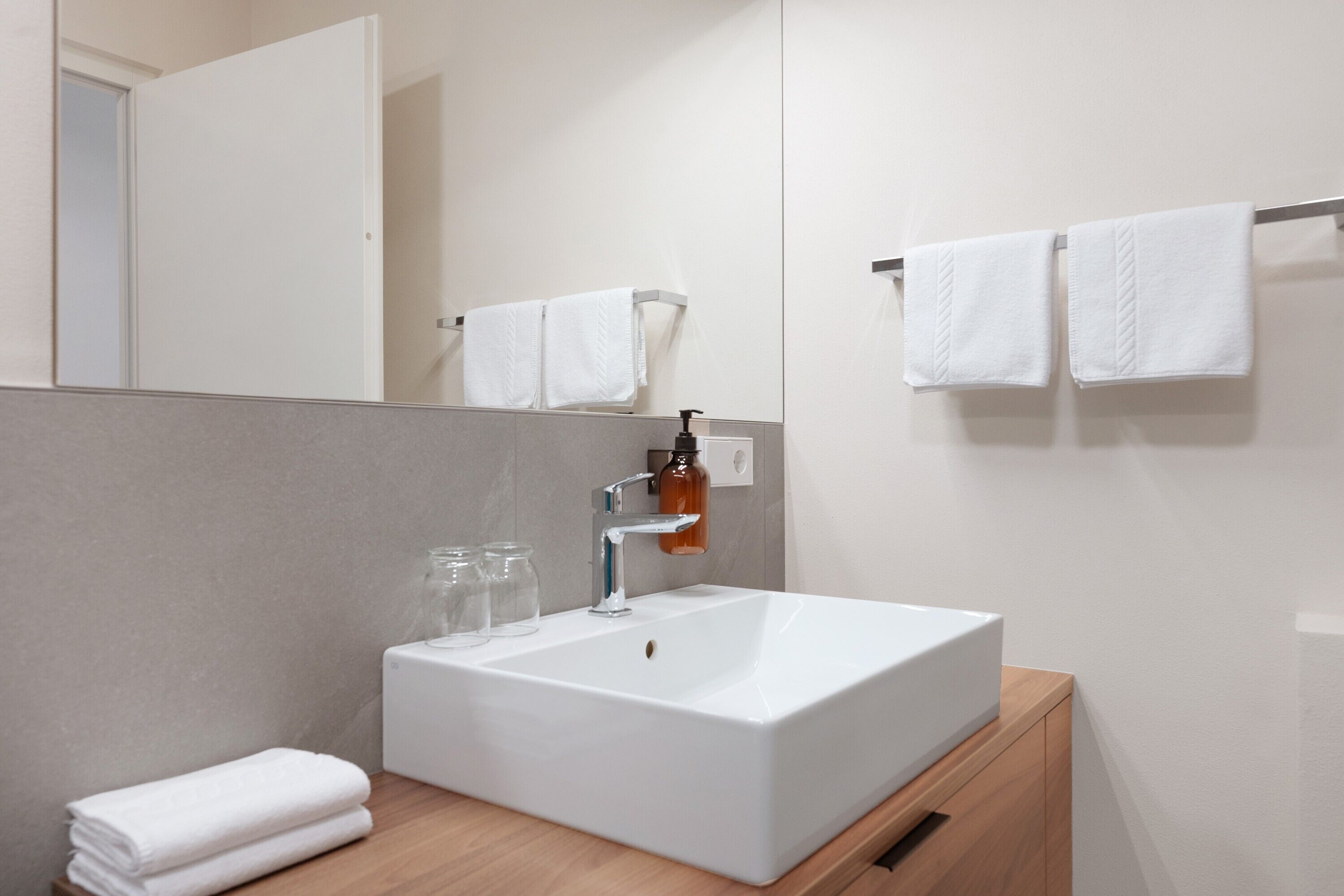 A modern bathroom with a white sink, a mirror, and two towels on a towel rack.