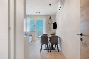 A modern dining area with a table and chairs, a pendant light, and a view through a glass door to a balcony. - Apartment 'Kanzi' with Mountain View, Large Outdoor Area & Pool (Lana)