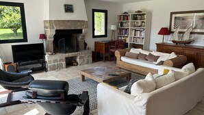 A living room with a stone fireplace, a bookshelf, a sofa, a coffee table, and a television. - KERALORH - Holiday home for rent in La Trinité sur Mer  - S1 (La Trinité-sur-Mer)
