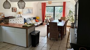 A spacious kitchen with a central island, dining area with wicker chairs, and a large window with red curtains. - KERALORH - Holiday home for rent in La Trinité sur Mer  - S1 (La Trinité-sur-Mer)