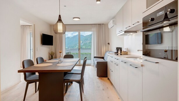 Eine moderne Küche mit Essbereich, einem an der Wand befestigten Fernseher und Bergblick durch das Fenster.