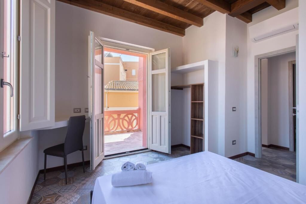 A hotel room with a bed, a chair, a wardrobe, and an open door leading to a balcony.