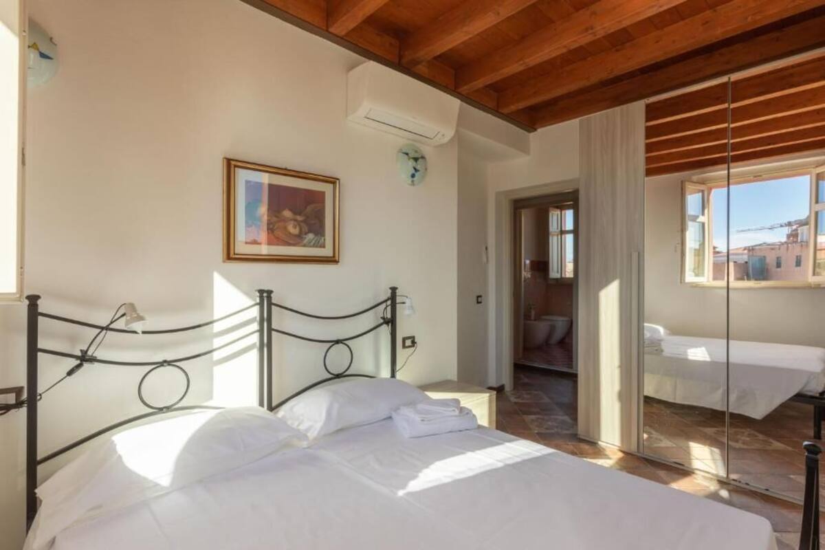 A bedroom with a bed, a painting, an air conditioning unit, and a view through a glass door.