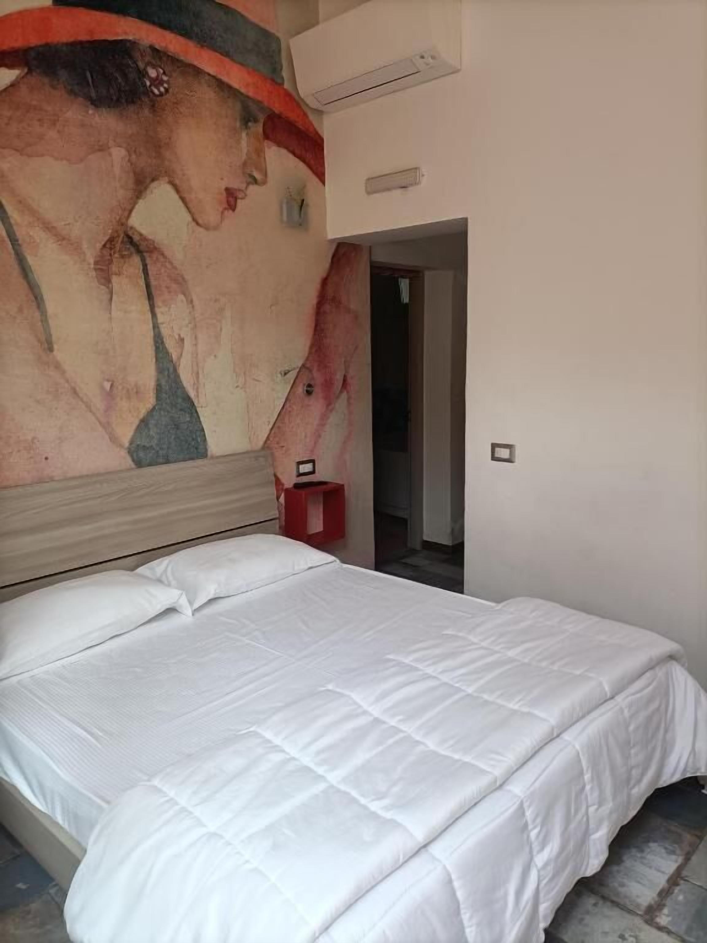 A bedroom with a large bed, a red nightstand, and a painting on the wall.