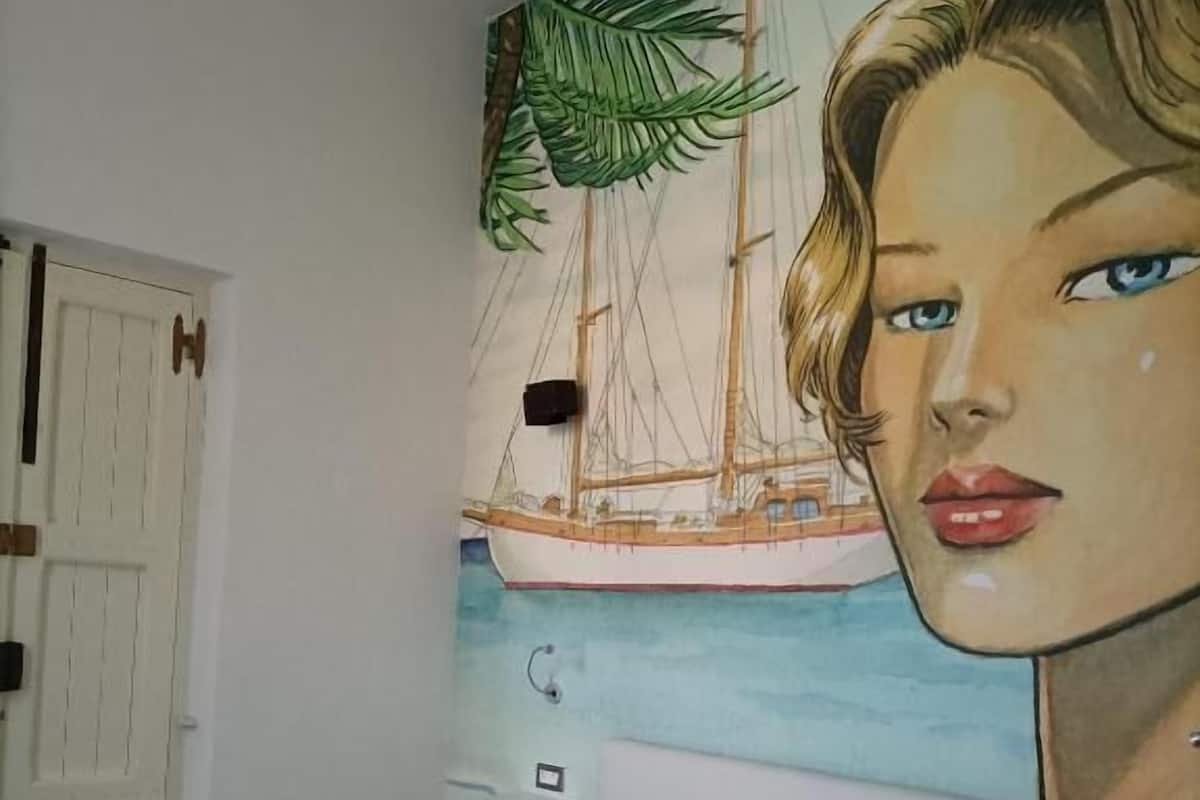 A bedroom with a bed, a white door, and a mural of a sailboat and a woman's face on the wall.