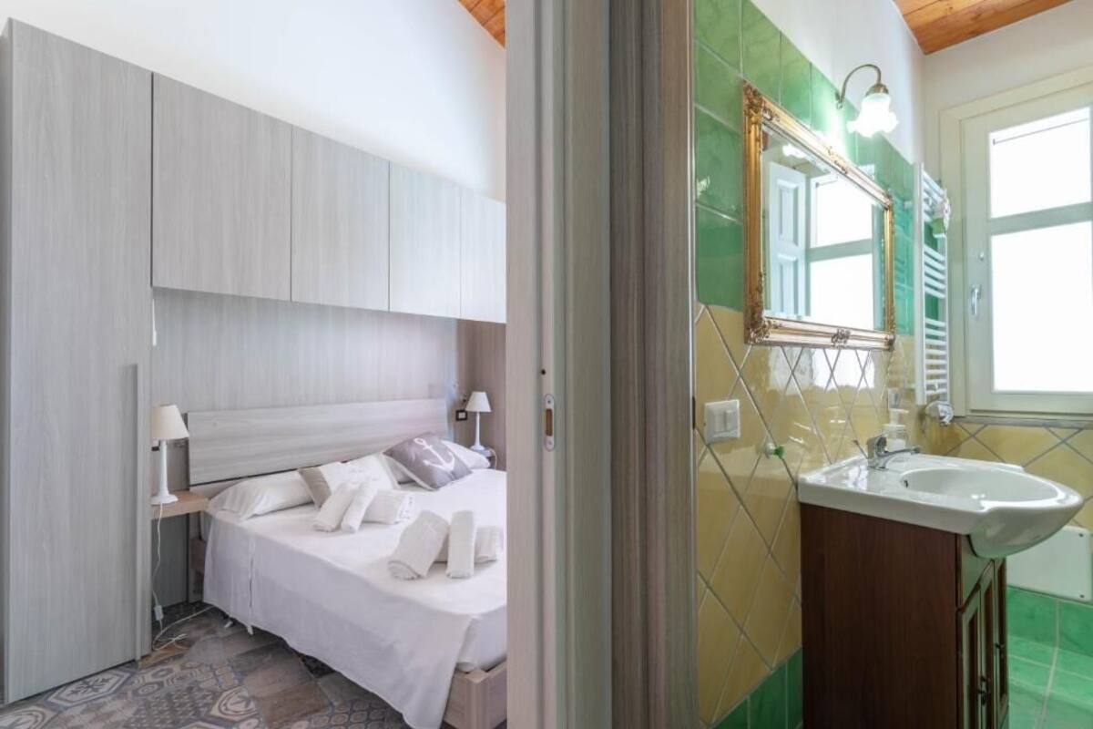 A hotel room with a bed, bedside table, lamp, and a bathroom with a sink and mirror.