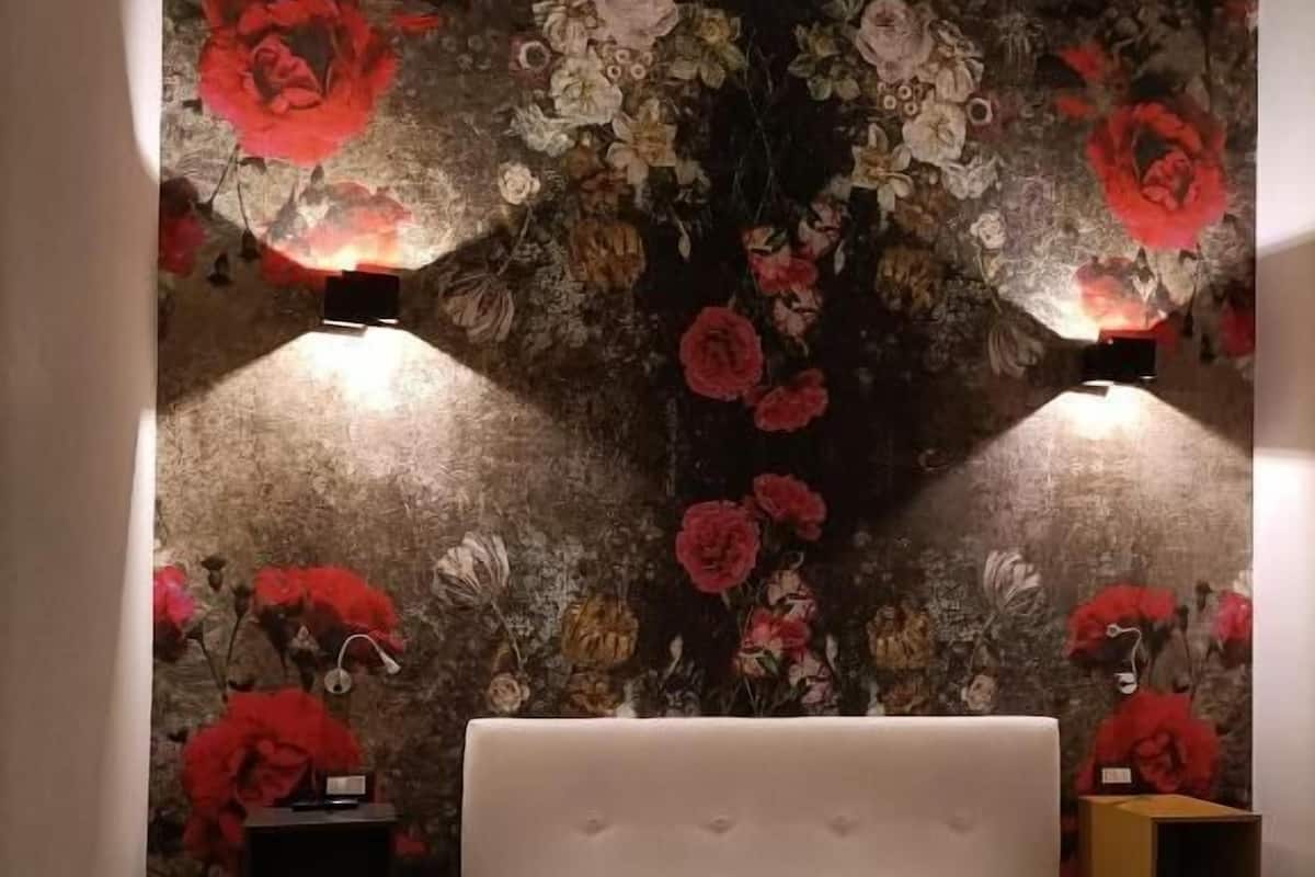A bedroom with a large bed, a floral wallpaper, two bedside tables with lamps, and a patterned floor.