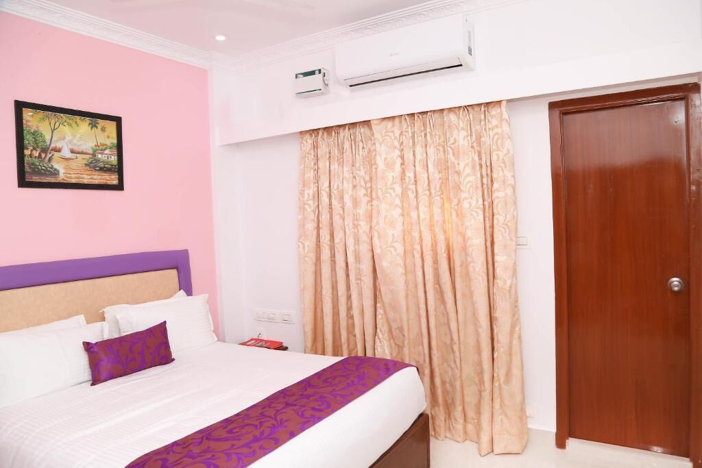 Una habitación de hotel con cama, un cuadro en la pared, un equipo de aire acondicionado, una puerta de madera y una cortina.