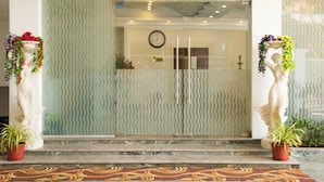 A hotel entrance with a textured glass door, a clock, and two statues with plants. - SBK Park Inn (Kanchipuram)
