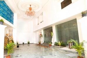A spacious lobby with a marble floor, a chandelier, and potted plants.