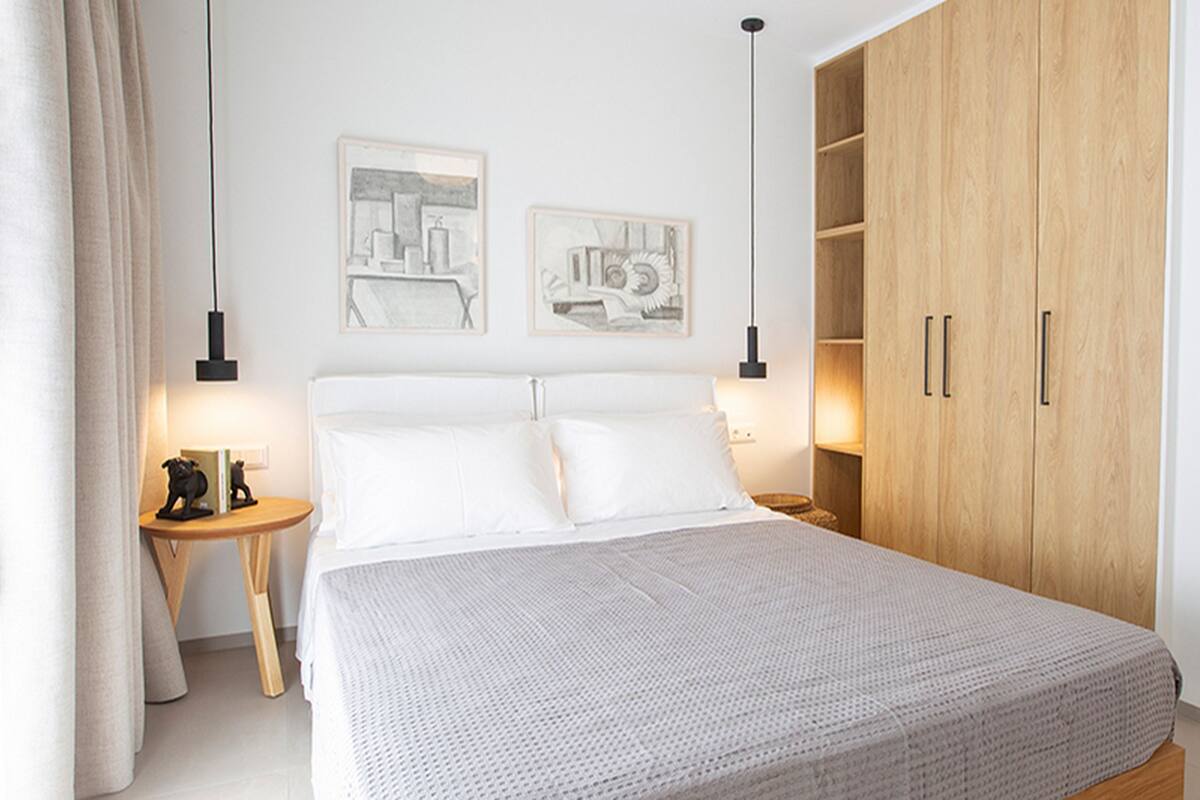Une chambre à coucher bien aménagée, avec un grand lit, deux œuvres d’art accrochées au mur, une armoire en bois et une table de chevet avec une lampe.