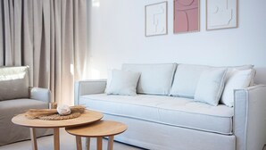 A modern living room with a light-colored sofa, a round wooden table, and a beige armchair. There are three framed artworks on the wall. - Lirides Suites (Lefkada)