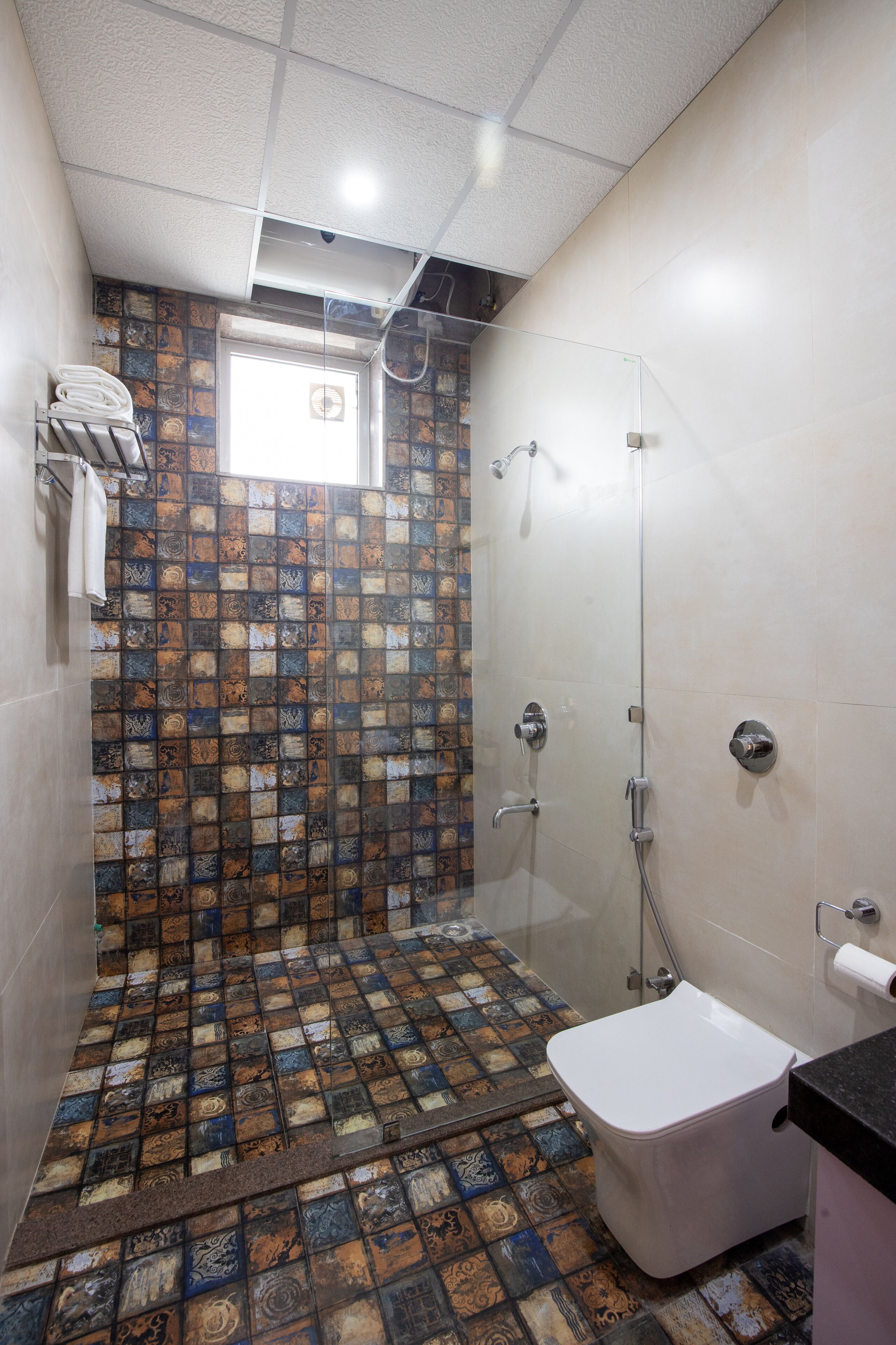 A shower area with a glass door, a white toilet, and a patterned tile floor.