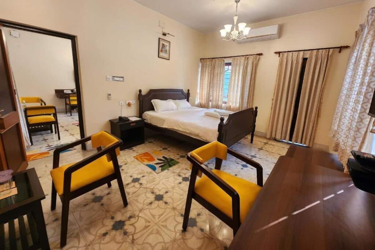 A hotel room with a bed, two chairs, a desk, a ceiling fan, and a chandelier.