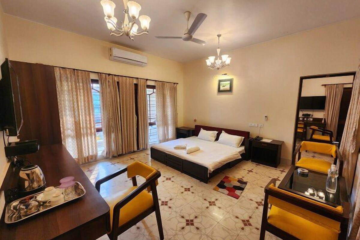 A hotel room with a bed, a desk with a chair, a small table, a ceiling fan, and a window with curtains.