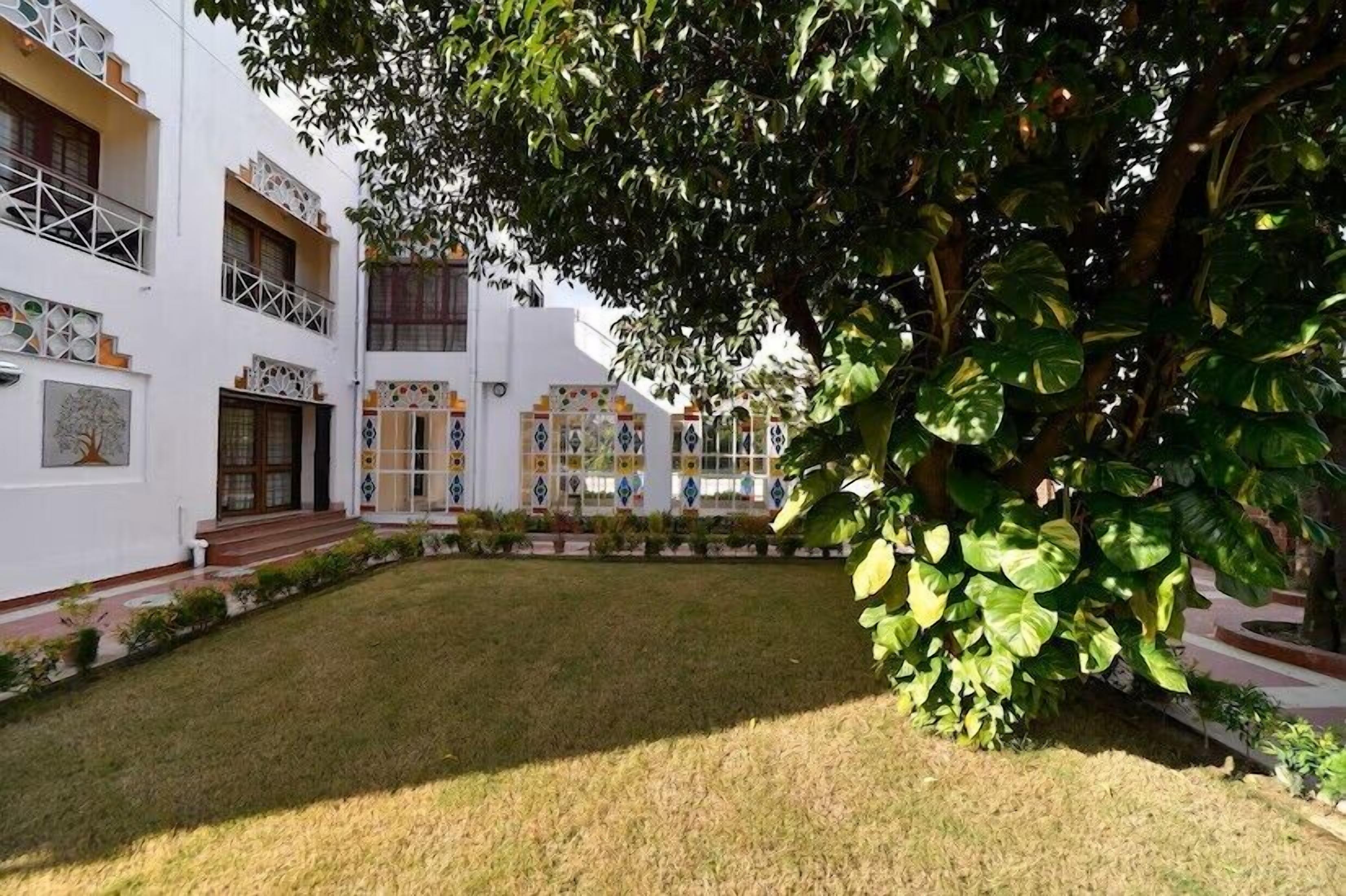 Um pátio com um edifício de fachada branca, várias janelas e um pequeno jardim.