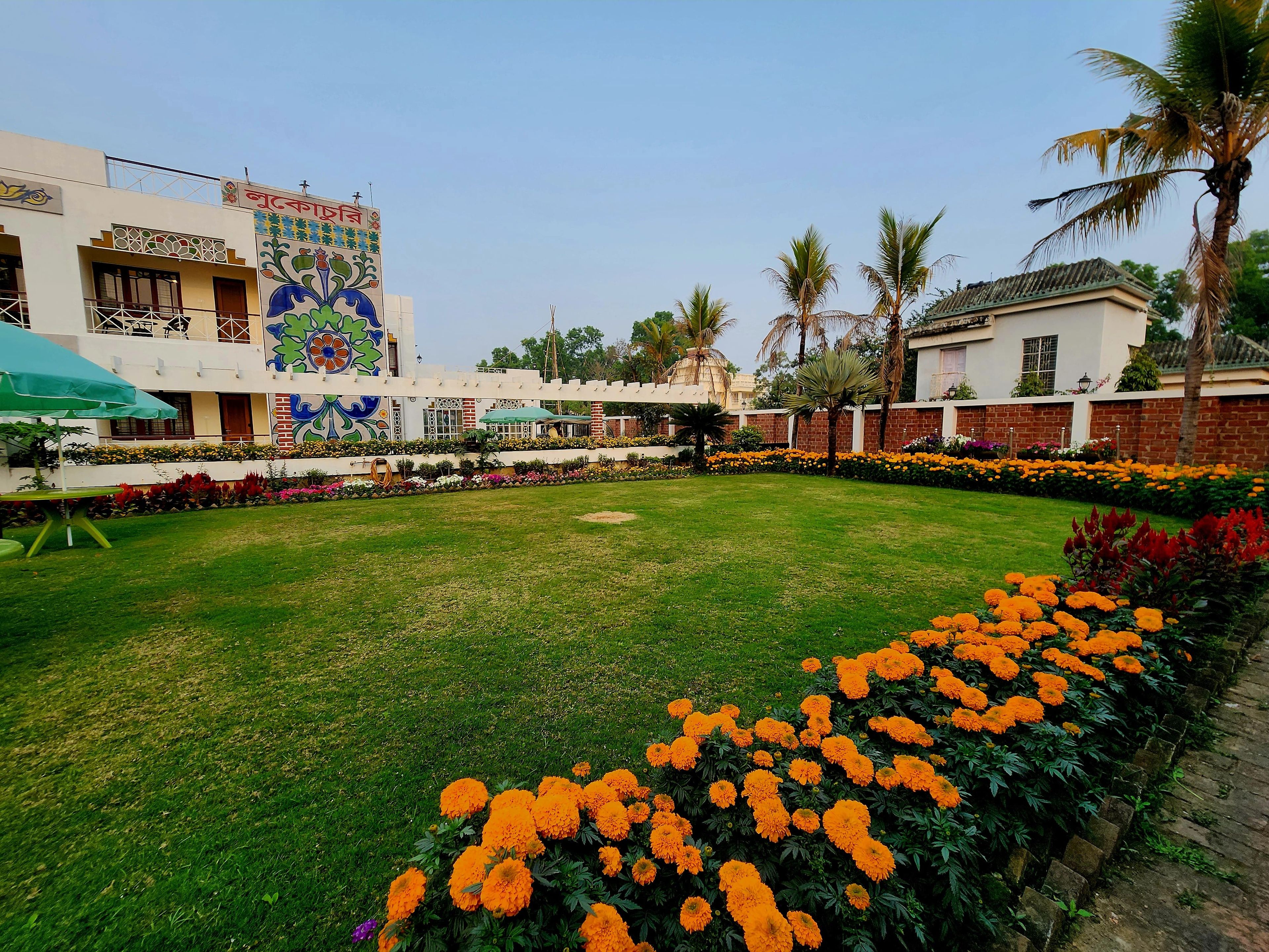 A courtyard with a lawn, a flower bed with marigolds, and a building with colorful murals.