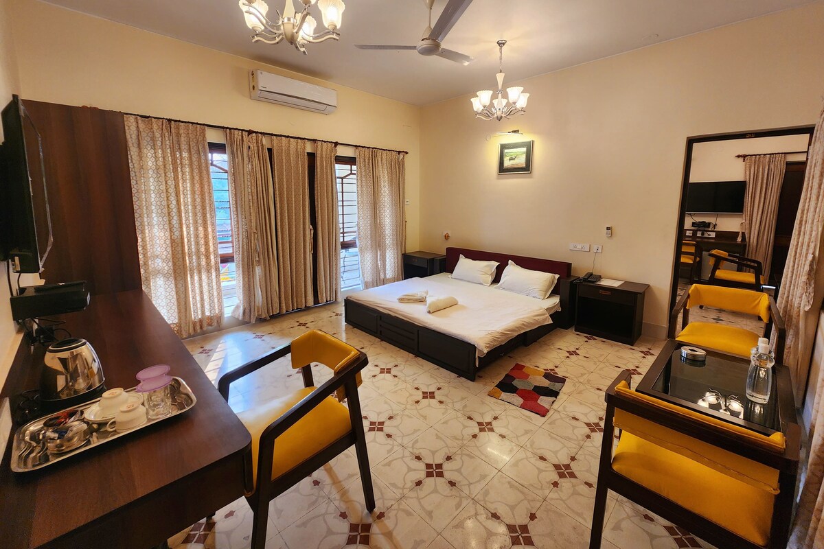 A hotel room with a bed, a desk with a tray of items, a chair, a ceiling fan, and a TV.