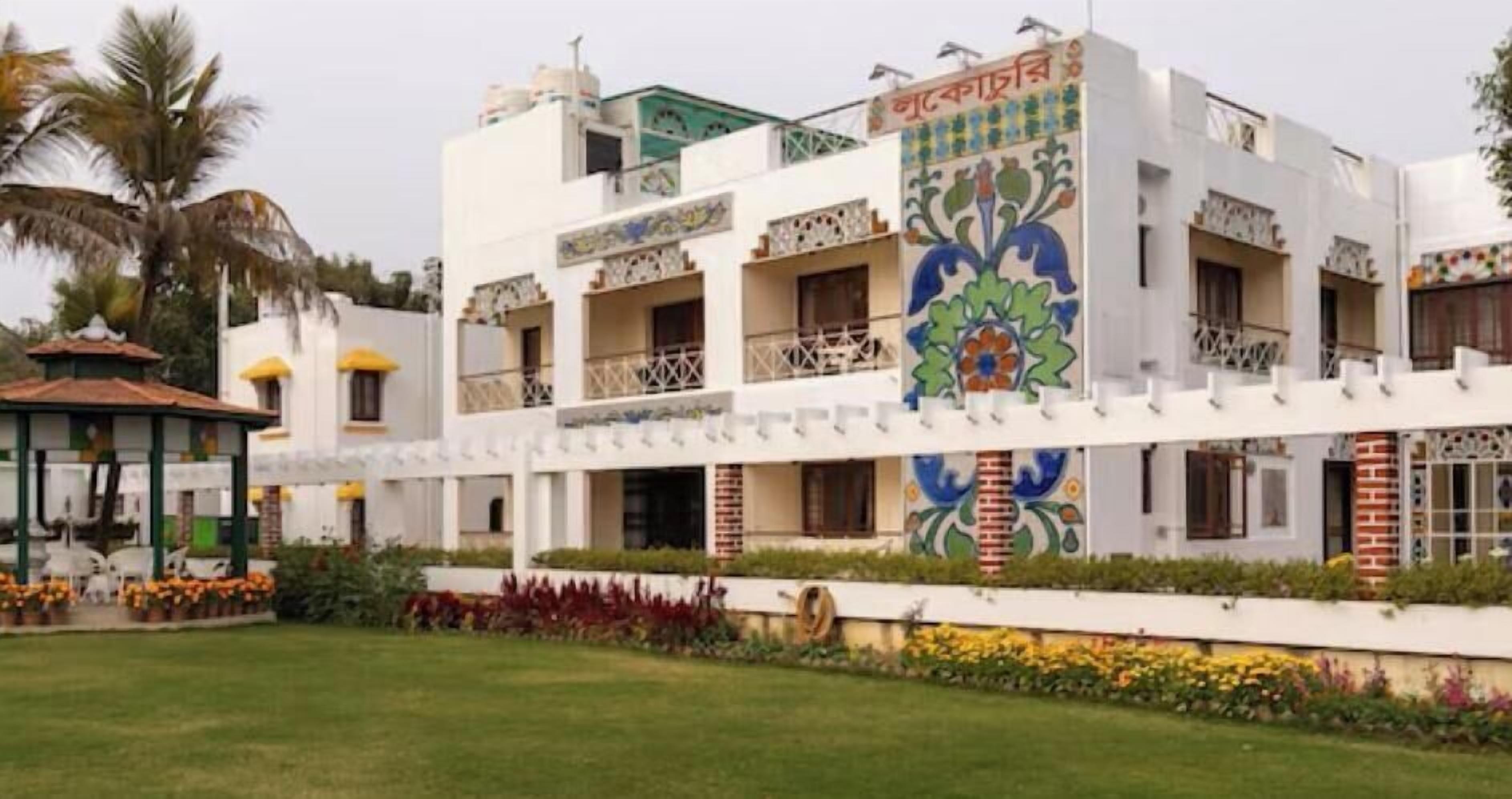 A multi-story building with balconies, a covered area with chairs, and a well-maintained lawn.
