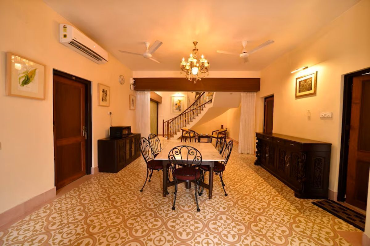 A dining room with a patterned carpet, a chandelier, ceiling fans, and a staircase leading to another level.
