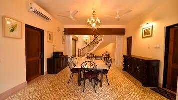 A dining room with a patterned carpet, a chandelier, ceiling fans, and a staircase leading to another level.