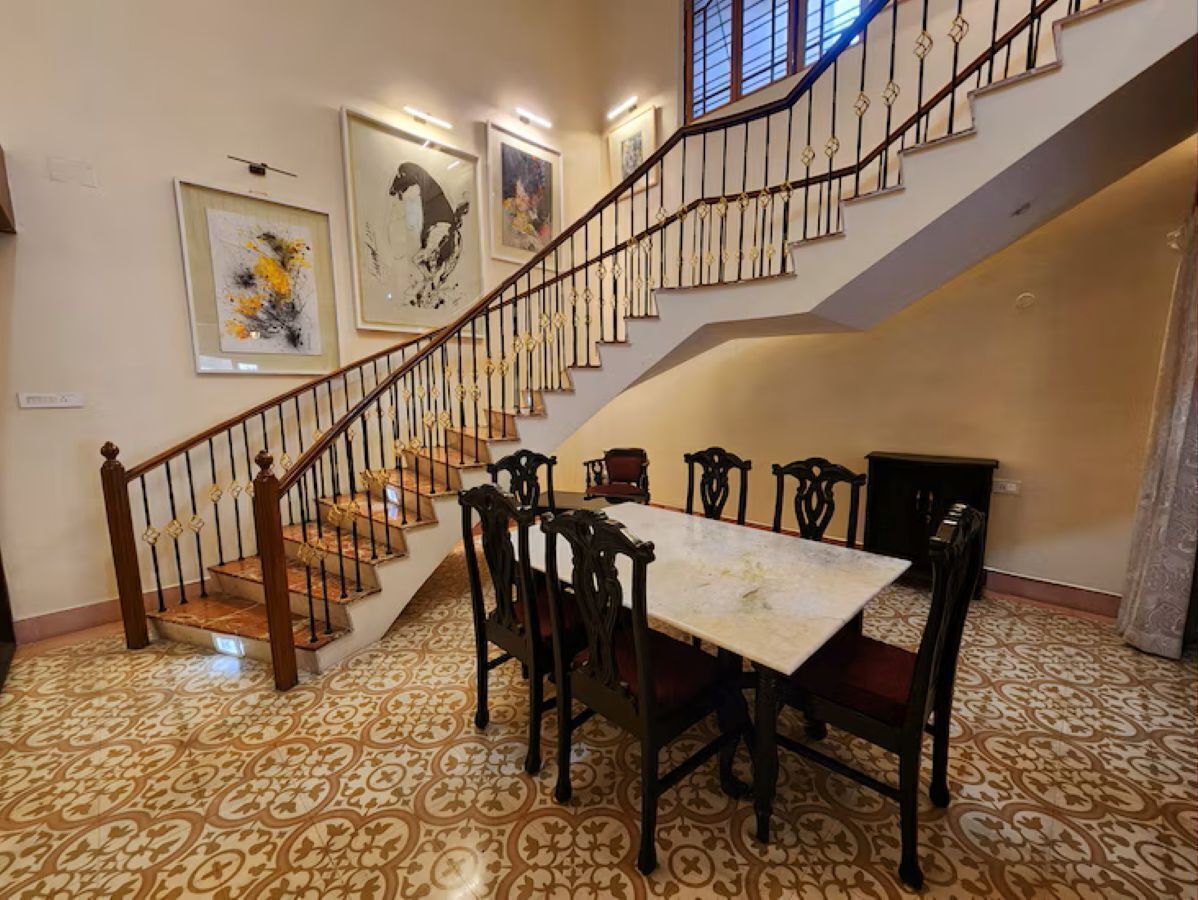 Un comedor con mesa y sillas, una escalera con barandilla y suelo estampado.
