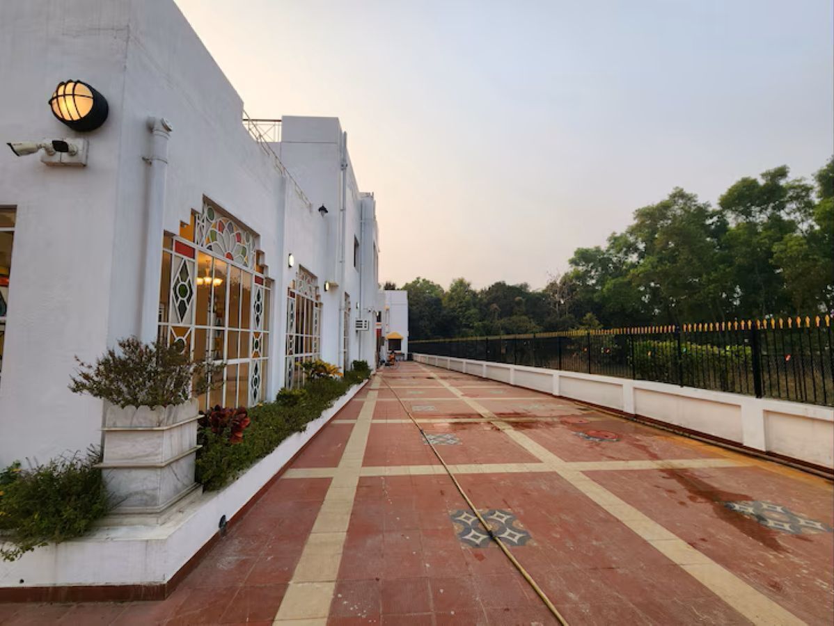 A pathway leading to a building with a white facade, a black metal fence, and a row of potted plants.