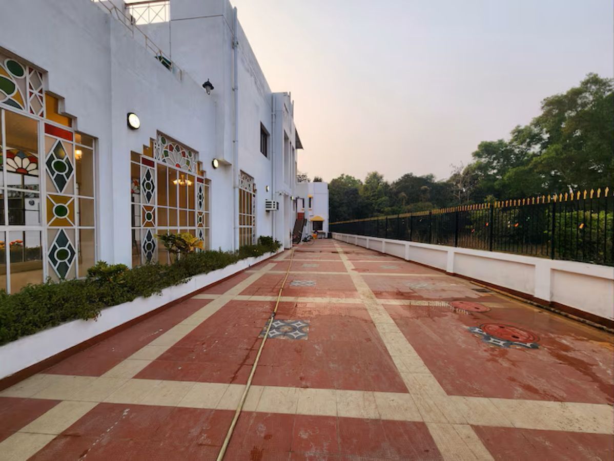 A corridor with patterned flooring, a white building with decorative windows, and a black fence.