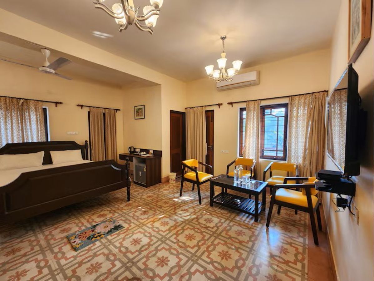 Una habitación de hotel con cama, escritorio, silla, televisor y ventana con cortinas.