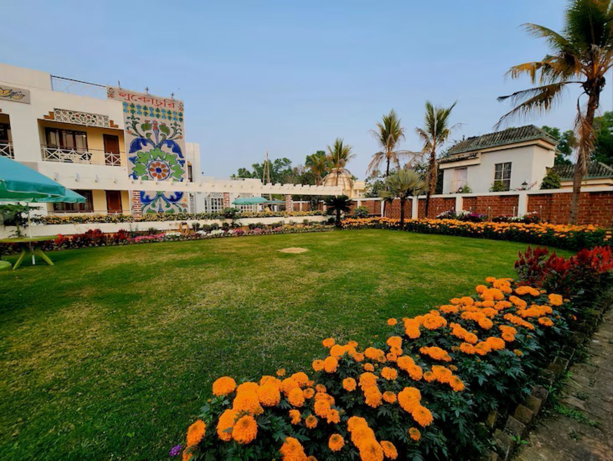 A courtyard with a lawn, a flower bed with orange flowers, and a building with a colorful mural.