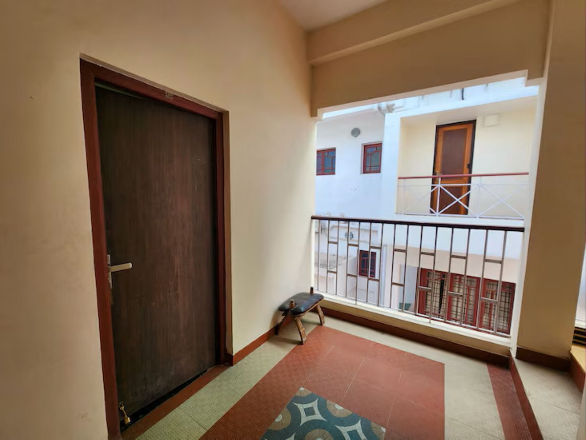 A balcony with a wooden door, a small bench, and a patterned rug.
