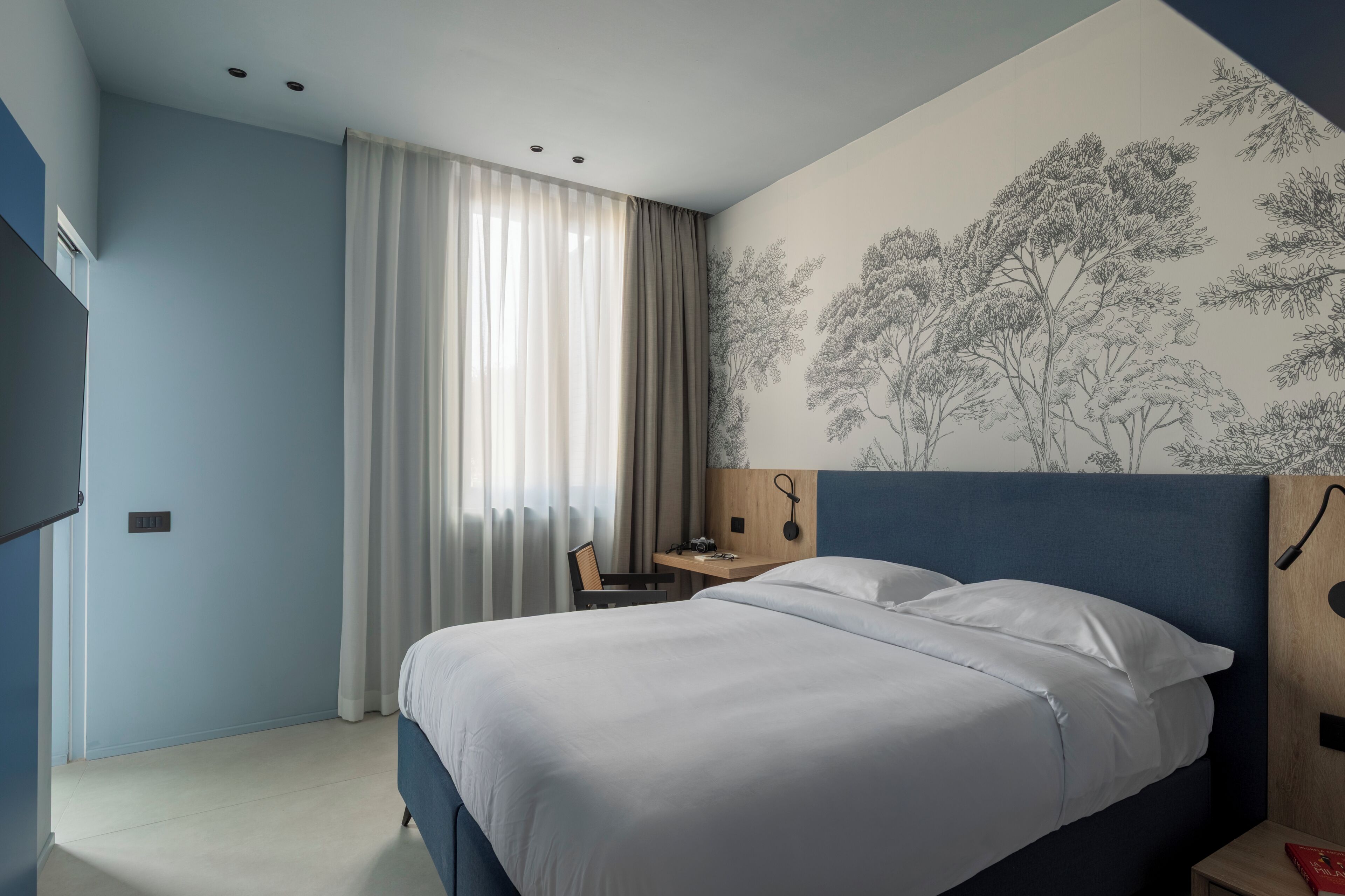 A bedroom with a bed, a desk, and a wall with a tree mural.