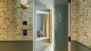 A hallway with a floral wallpaper, a door with a keyhole, a chair, and a desk with a lamp.