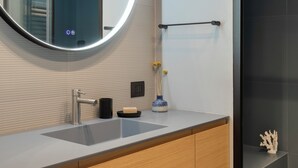 A modern bathroom with a round mirror, a sink, a towel rack, and a glass shower enclosure.