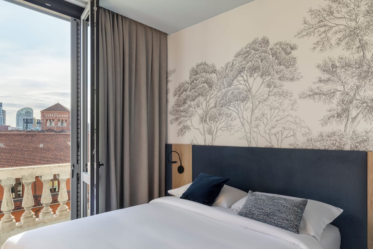 Une chambre d’hôtel avec un lit, une vue sur le paysage urbain et un mur orné d’une fresque représentant un arbre.