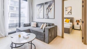 A modern living room with a grey sofa, a round coffee table, and two abstract paintings on the wall. - Premium 1BR with Great Amenities in JVC (Dubai)
