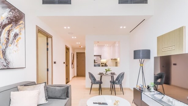 A modern living room with a sofa, coffee table, and dining area. There is a kitchen in the background with a dining table and chairs. - Premium 1BR with Great Amenities in JVC (Dubai)