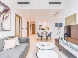 Ein modernes Wohnzimmer mit einer Couch, einem Couchtisch und einem Essbereich. Im Hintergrund befindet sich eine Küche mit Esstisch und Stühlen.