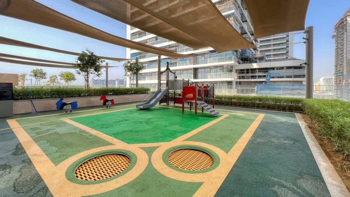 Un parque infantil al aire libre con toboganes y columpios, rodeado de vegetación y edificios modernos.