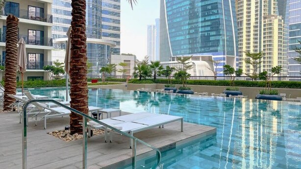 Ein moderner Poolbereich mit Liegestühlen, Palmen und Hochhäusern im Hintergrund.
