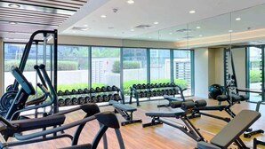 Ein modernes Fitnessstudio mit verschiedenen Trainingsgeräten, großen Fenstern und Blick auf Grünflächen.