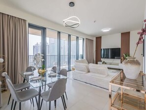 A modern living room with a glass dining table, white sofa, and a large window with a city view. - Luxury 2BR Family Living - Premium Amenities (Dubai)