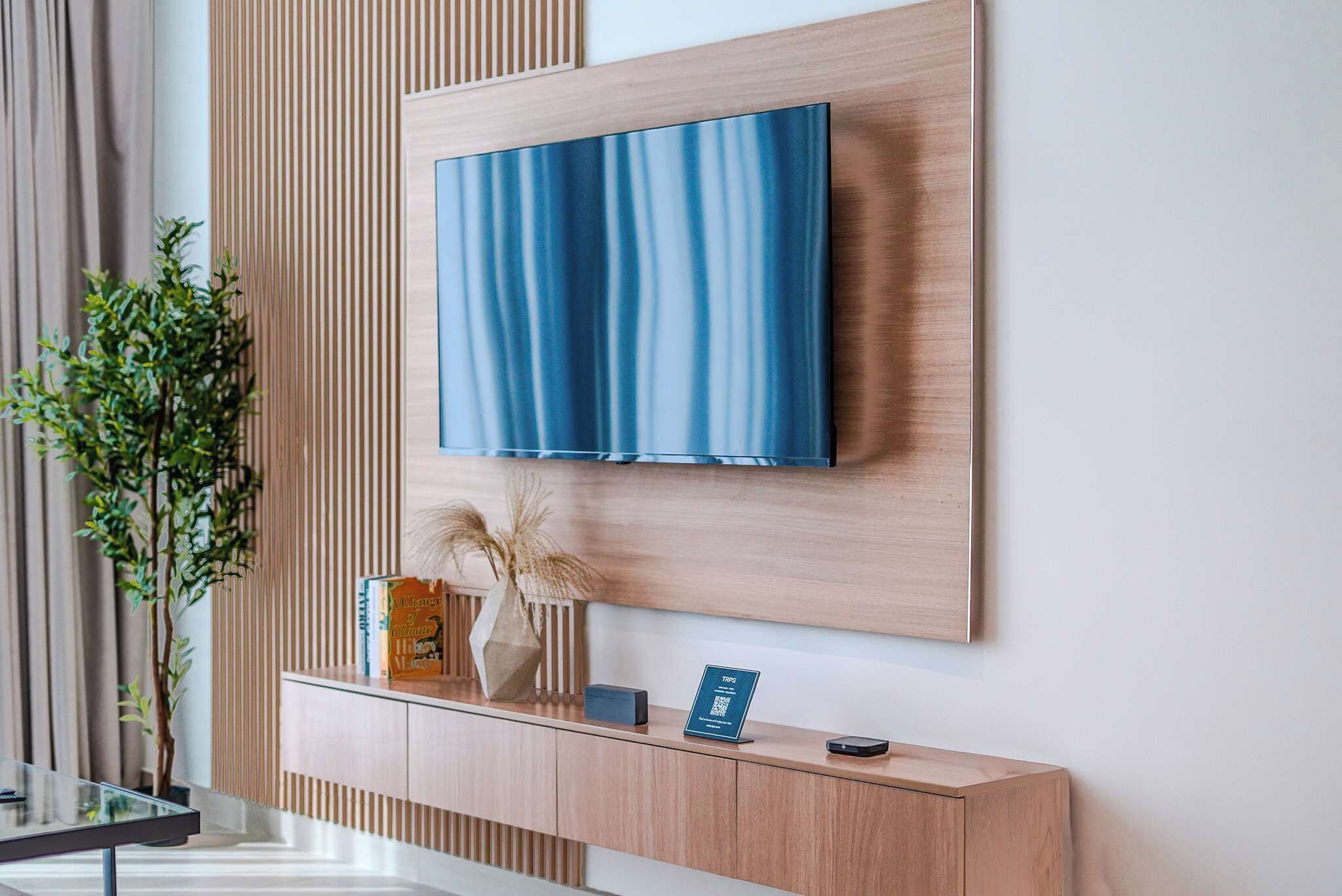 Un espace d’accueil moderne, avec un comptoir en bois, un téléviseur fixé au mur et une plante en pot.