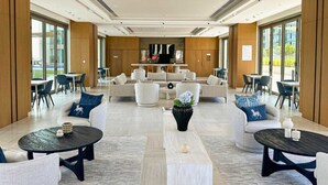 Eine großzügige Lobby mit modernem Design, mit einer zentralen Sitzecke mit Sofas und Sesseln, umgeben von Esstischen und Stühlen.