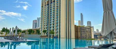 A modern hotel with a rooftop pool, high-rise buildings in the background, and a clear sky.