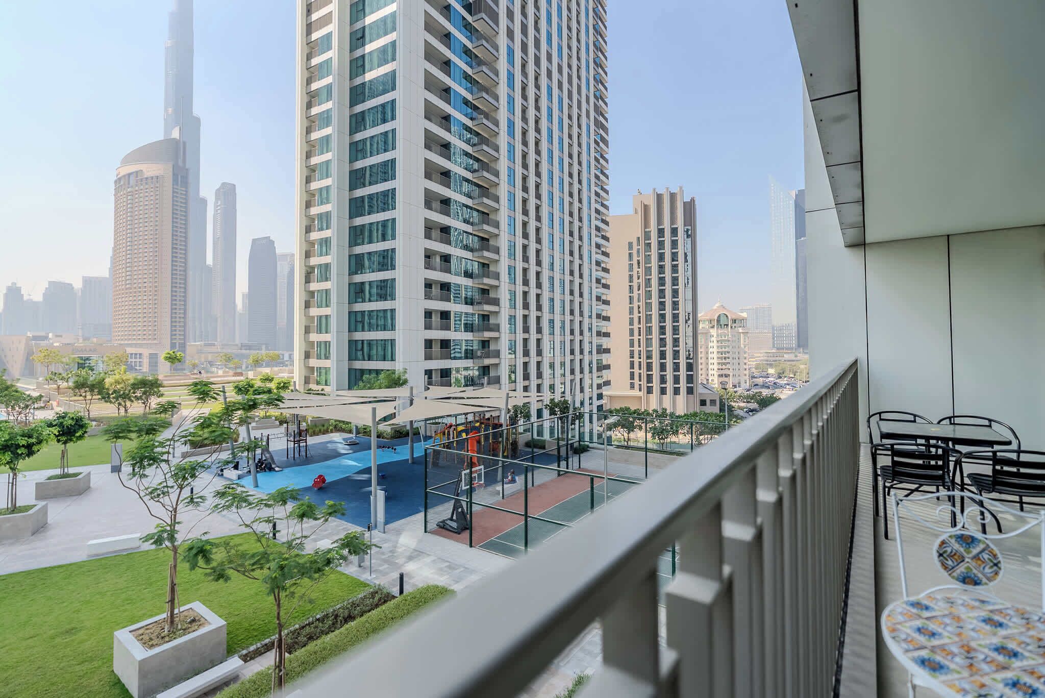 A high-rise building with a view of a swimming pool and park area.