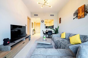 A modern living room with a flat-screen TV, grey sofas, a coffee table, and a dining area in the background. - Pool View, Fully Furnished, Prime JVC Location (Dubai)