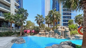 Una piscina con diseño de roca natural, rodeada de palmeras y edificios modernos.