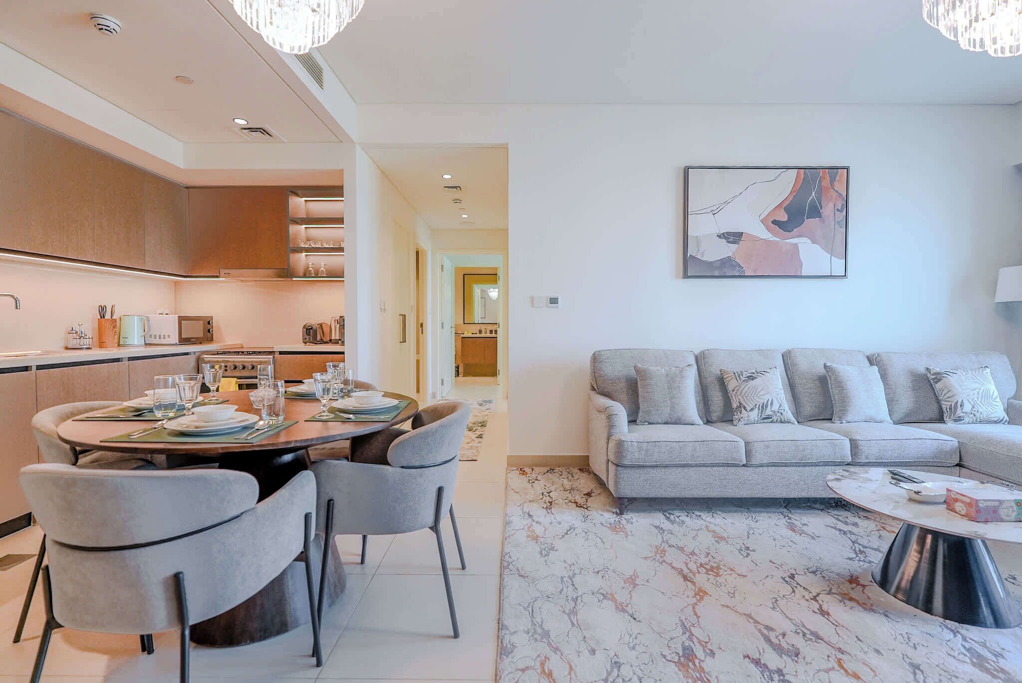 A modern living room with a grey sofa and a dining area with a round table and chairs.